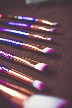 A collection of beautifully crafted makeup brushes with metallic handles, arranged in soft shallow focus.