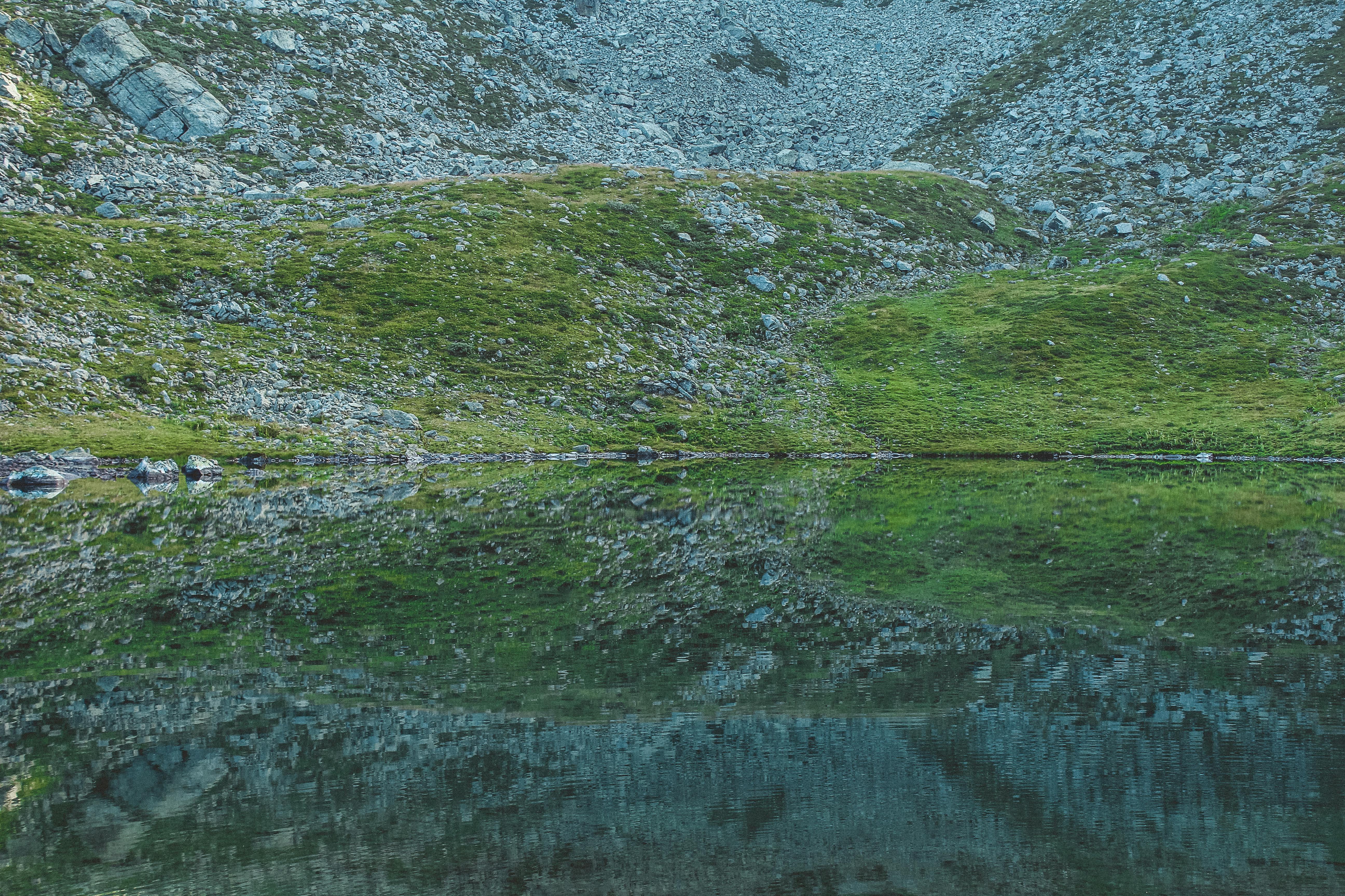 宁静的户外场景中，湖面映照出山坡上的岩石和草地
