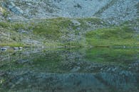 宁静的户外场景中，湖面映照出山坡上的岩石和草地