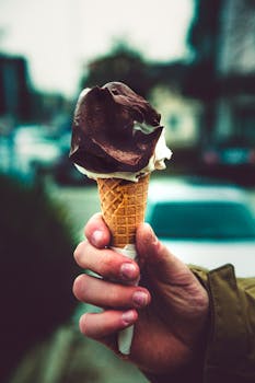 Close-up of a hand holding a chocolate ice cream cone outdoors.