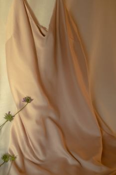 A sophisticated beige silk dress draped elegantly against a soft backdrop with delicate floral accents.