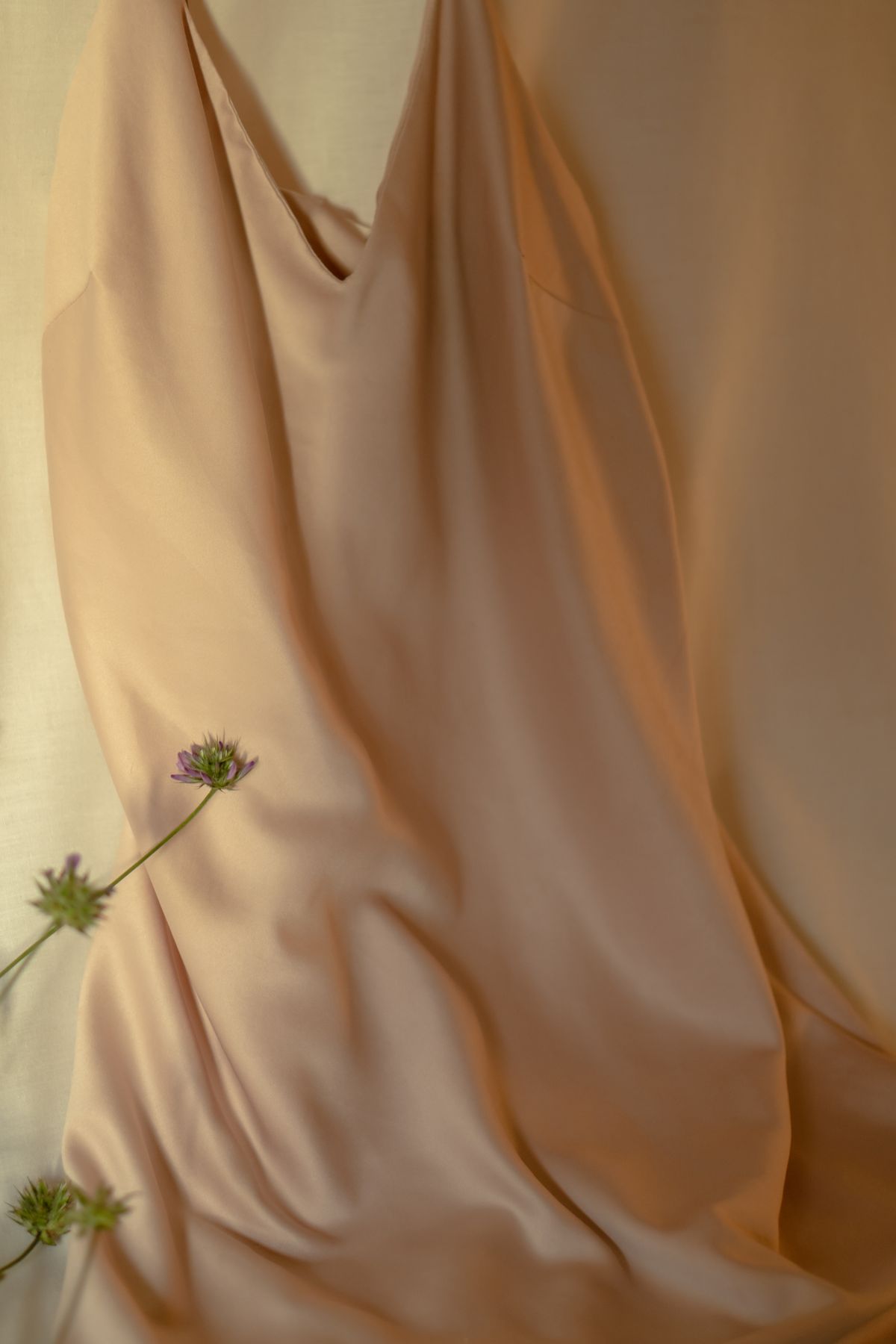 A pale silk dress laid flat with cut stems beside it