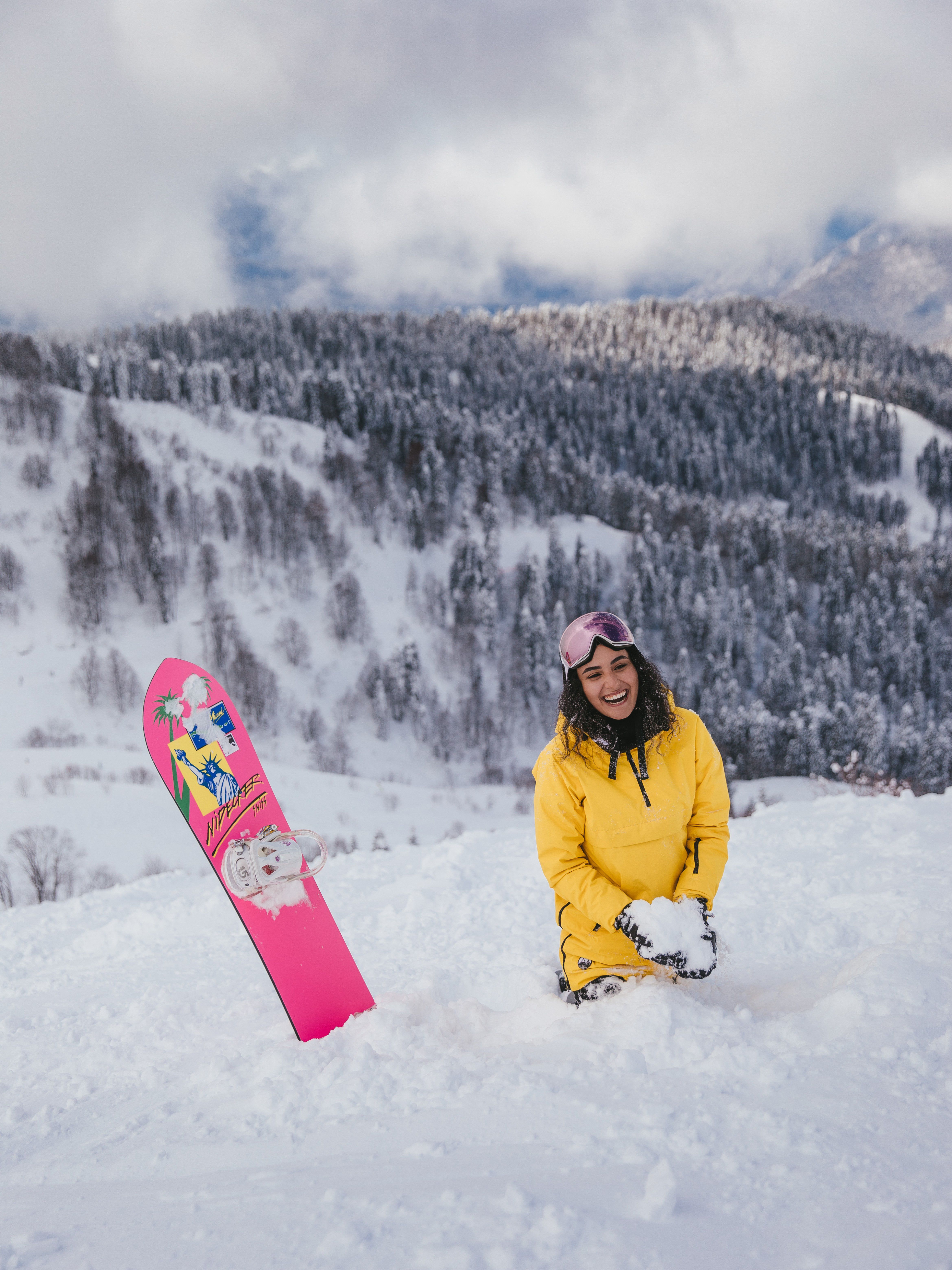 A cheerful woman enjoys snowboarding in a vibrant yellow jacket on a snowy mountain.