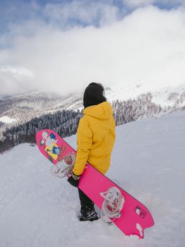 Woman in a yellow jacket snowboarding on a snowy mountain peak during winter day.