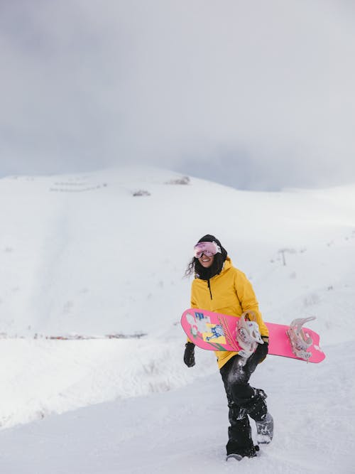 Woman in Yellow Hoodie Holding Pink and White Snowboard