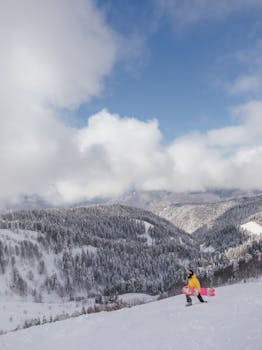 Snowboarder in yellow jacket on a snowy mountain with a scenic winter landscape.
