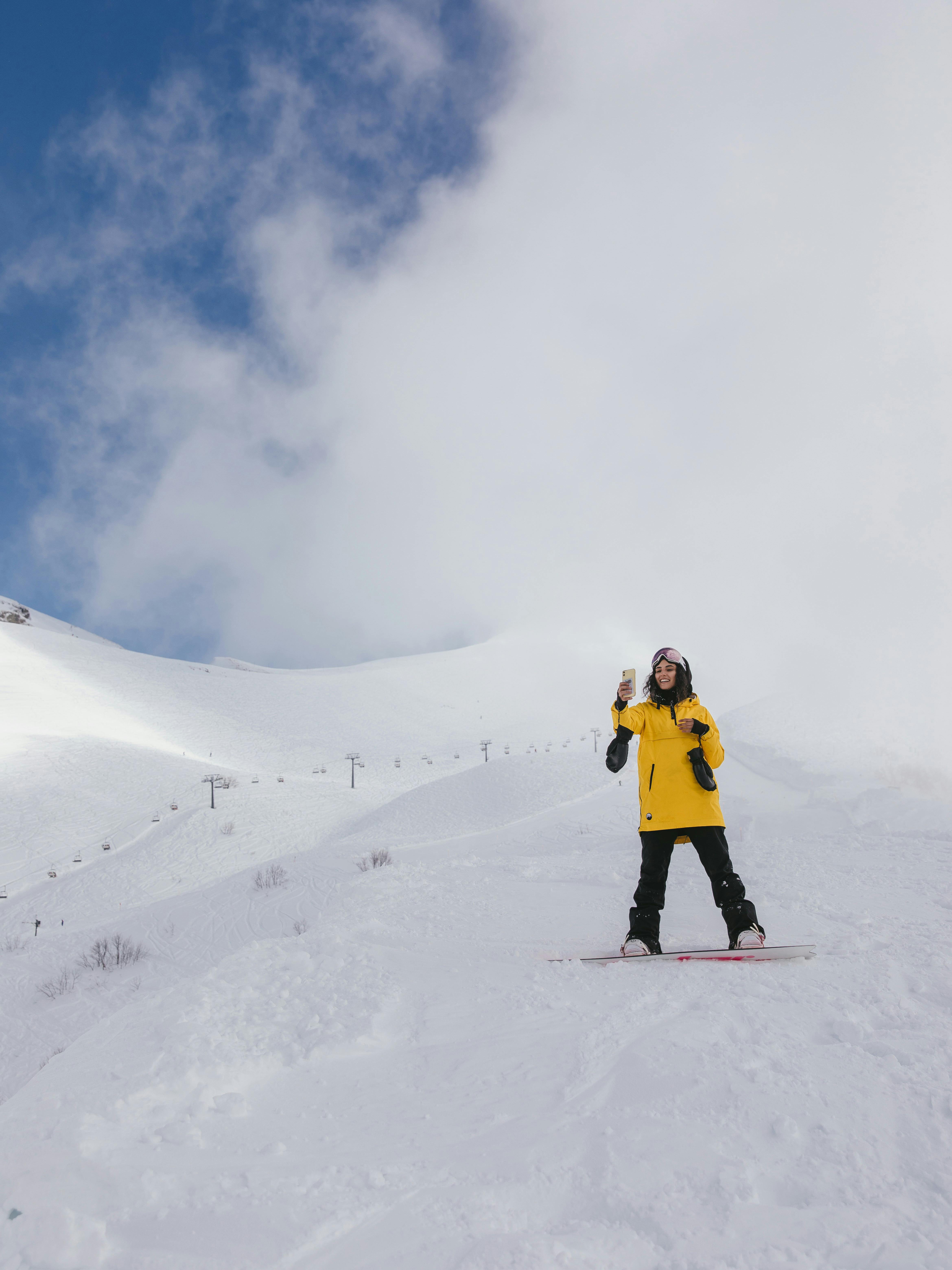 Prescription Goggle Inserts - Snowboarder in a yellow jacket posing on a snowy mountain with clear blue skies.