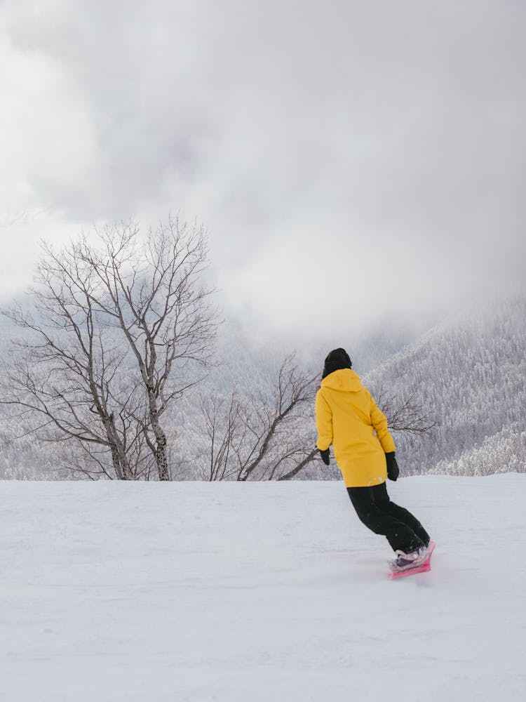 A Person Wearing Yellow Jacket While Snowboarding 