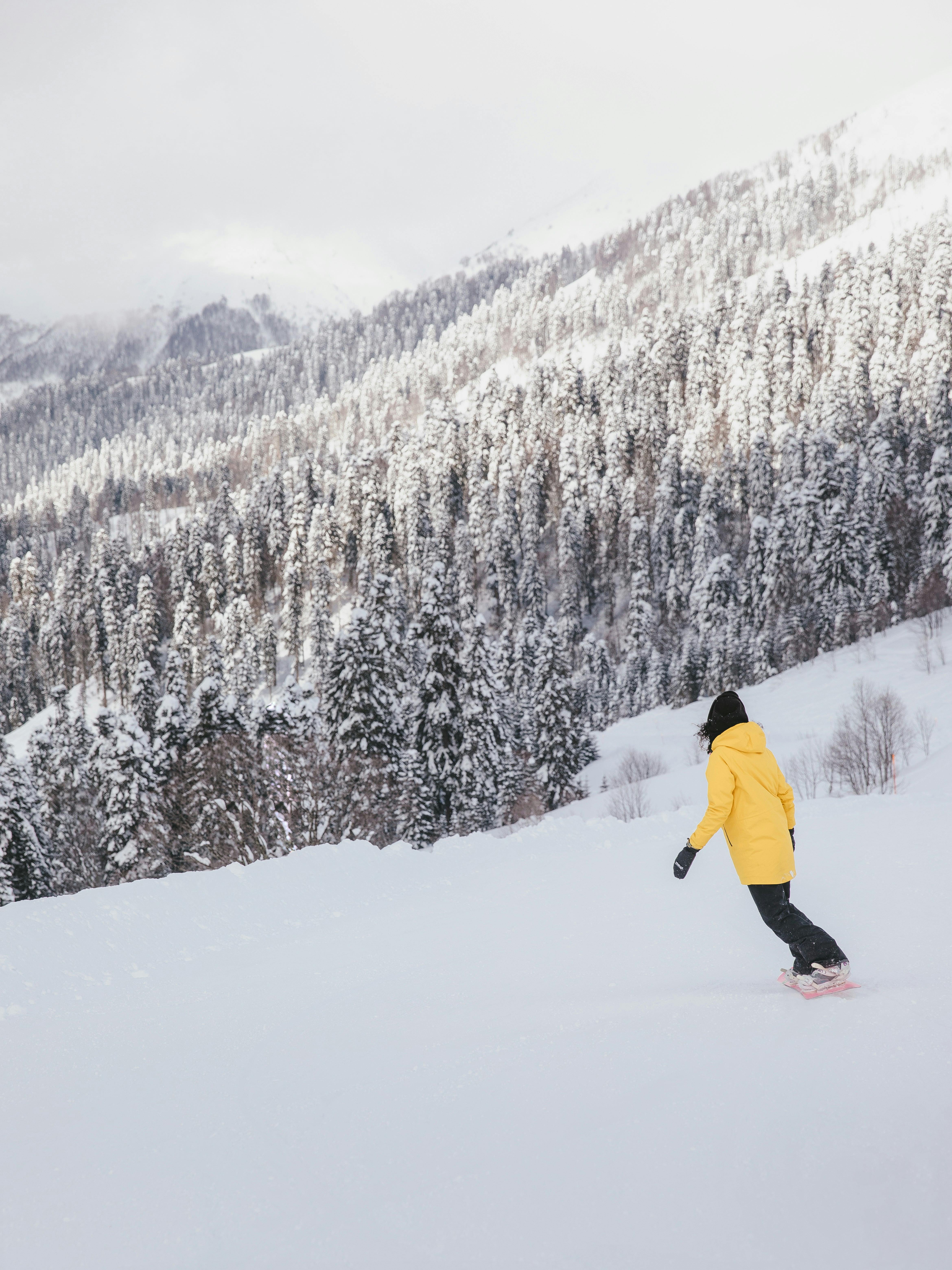 Snowboarder in yellow attire descends a snowy mountain slope surrounded by pine trees.