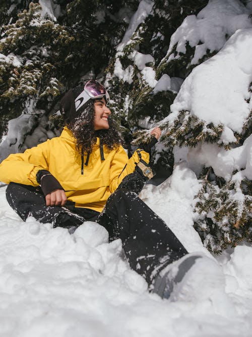 Smiling Woman in Winter Clothing Sitting near the Pine Tree