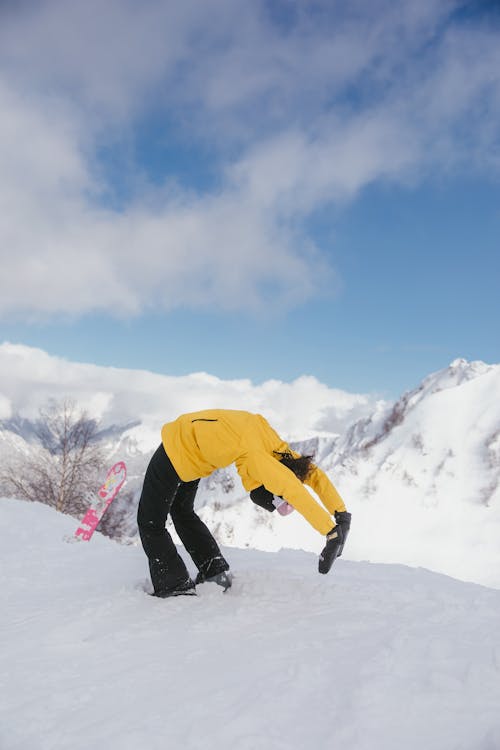 A Person in Winter Clothing Bending Her Body on Snow-Covered Ground