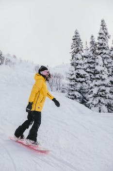 Woman enjoying a snowboarding ride down a snowy mountain, wearing a yellow jacket, in a winter wonderland.