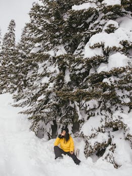 A woman in a yellow jacket enjoying the snowy forest landscape during winter.