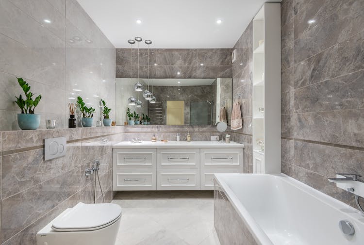 Spacious Bathroom With Bathtub And Mirror Hanging Over White Cupboard