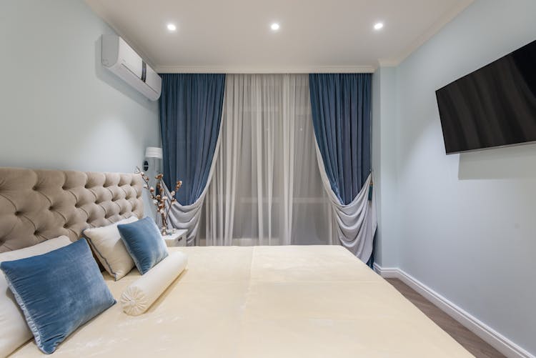 Interior Of Cozy Bedroom With Soft Bed And Blue Cushions And Curtains