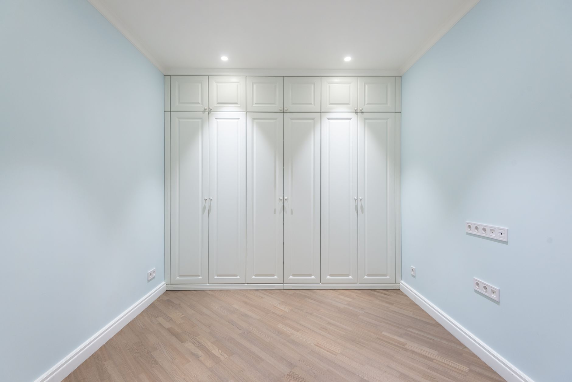 Empty spacious room with parquet floor and built in wardrobe with white doors under glowing lamps