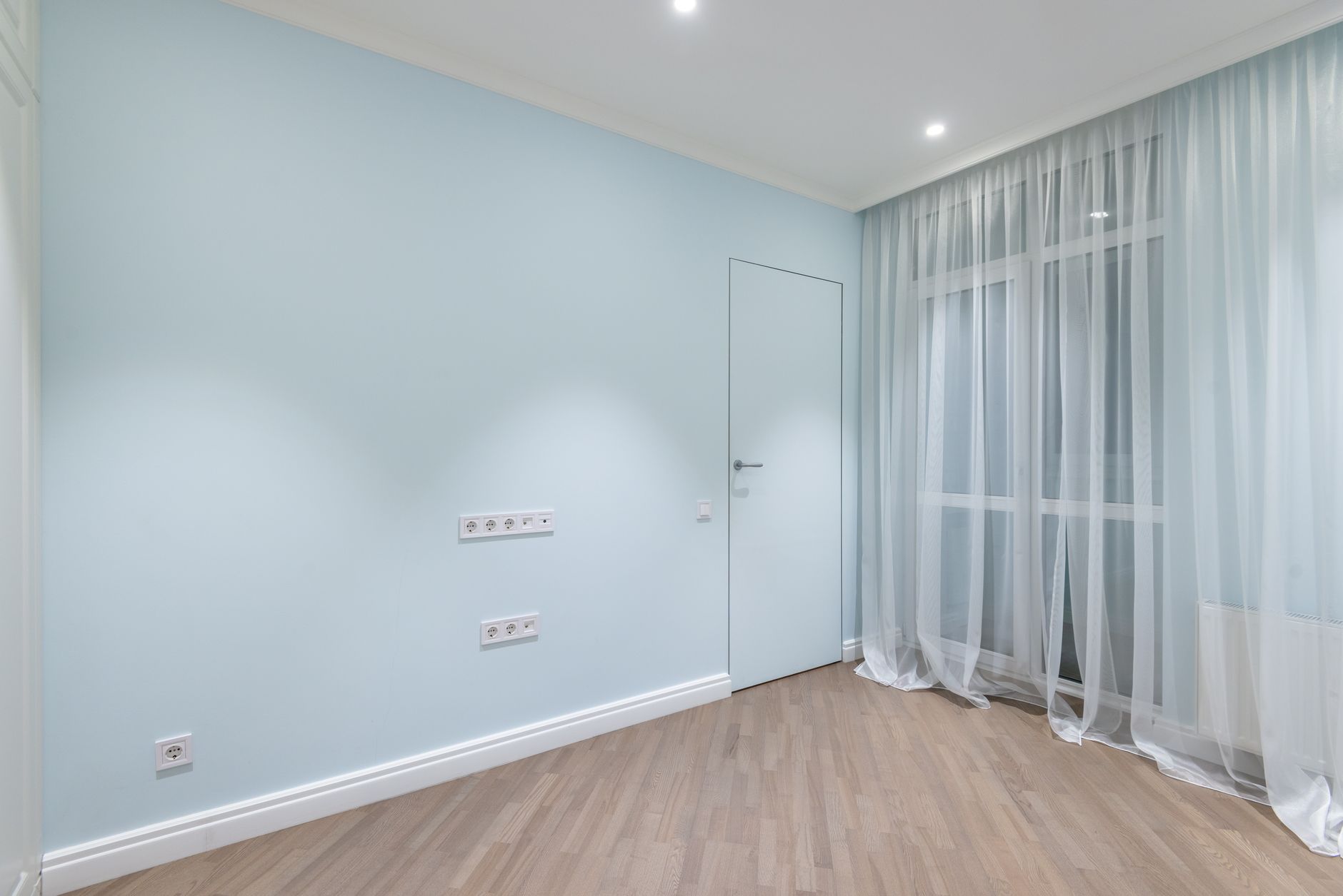 新成屋全室窗簾預算怎麼抓?從房型快速估範圍 A modern, minimalist empty room with light blue walls and sheer curtains, offering a clean and spacious atmosphere.