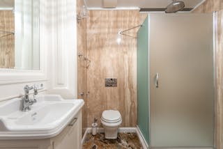 Interior of bathroom with wall mounted toilet and shower cabin at tiled wall near clean sink under bright lighting