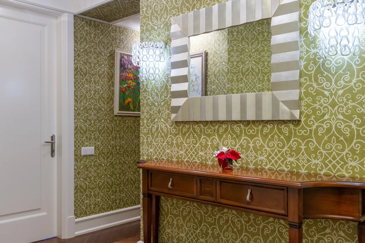 Wooden console table with drawers under a large mirror in a patterned hallway