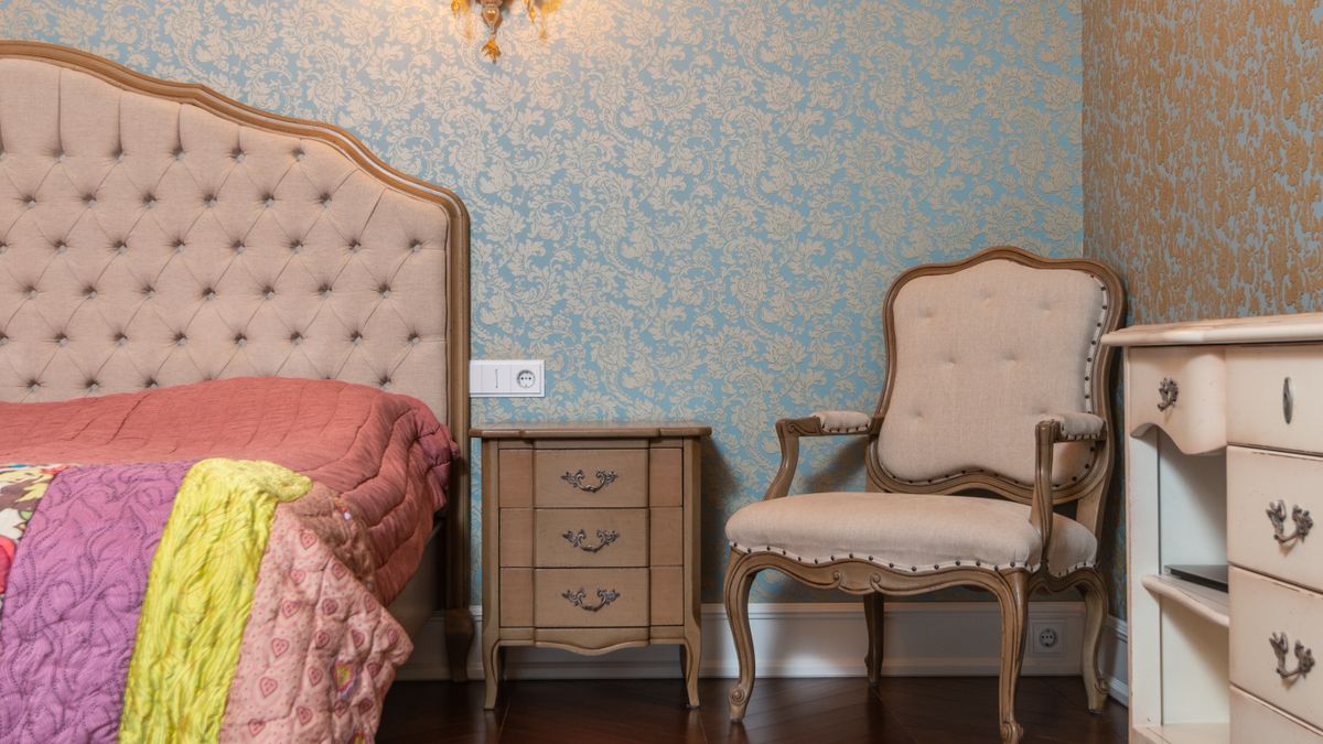 A bedroom with patterned wallpaper and vintage furniture.