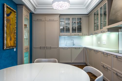 Free Contemporary indoor kitchen featuring elegant cabinetry and a glass top table with chandelier lighting. Stock Photo