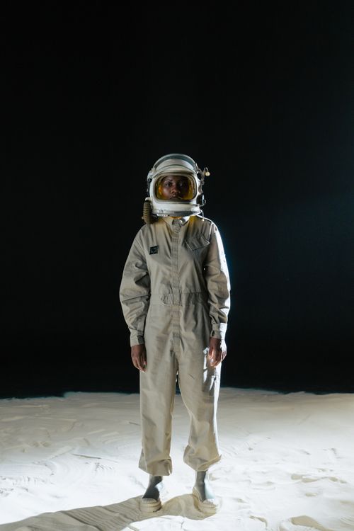 Free Astronaut standing in spacesuit on moon-like surface with black background. Stock Photo