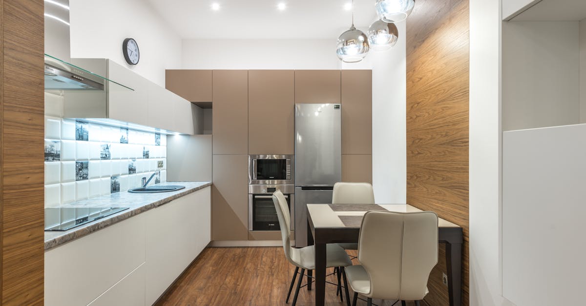 Modern kitchen interior featuring sleek cabinetry, stainless steel appliances, and a dining table with chairs, emphasizing space efficiency and contemporary design.