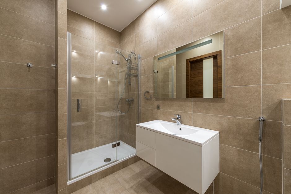 Elegantly designed modern bathroom featuring a glass shower, wall mirror, and large ceramic tiles.