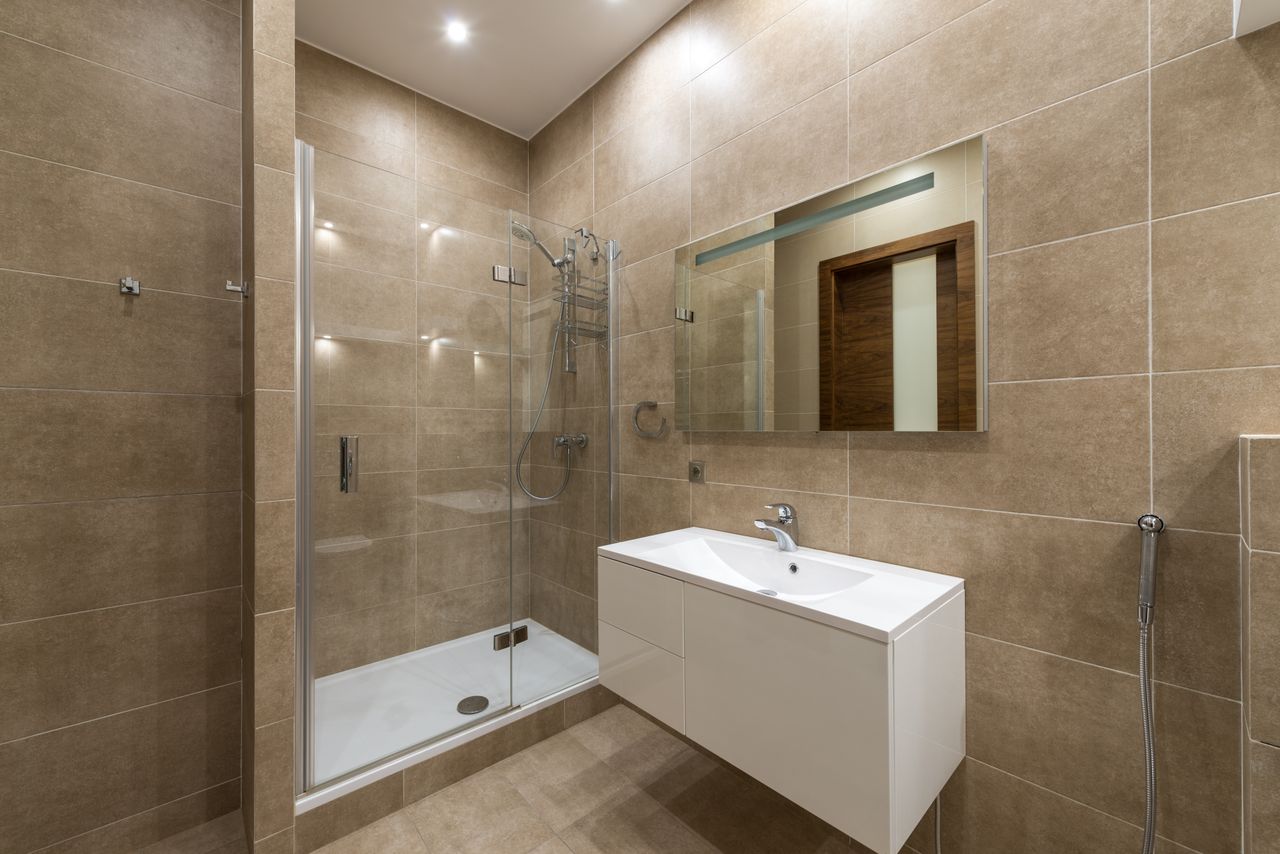 Large-format beige tiled bathroom with a glass shower and a floating vanity