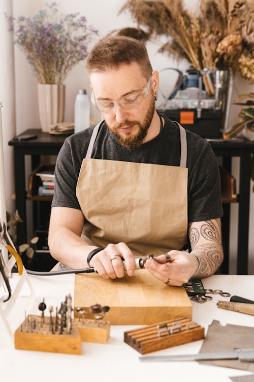 A Man Wearing Protective Goggles and Brown Apron Holding a Grinder