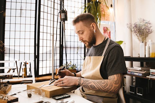 A Man Wearing Brown Apron Holding a Pen on a Wooden Board