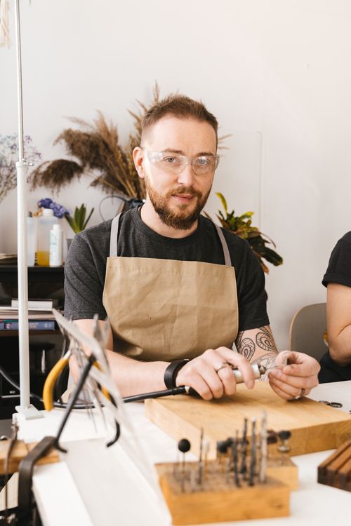Free Tattooed craftsman wearing apron and goggles working on tools at a workshop desk. Stock Photo