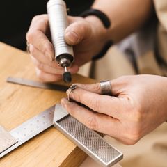 Hands smoothing a ring with a rotary tool at a wooden workbench