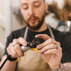 A craftsman in a yellow and black apron using a flex-shaft rotary tool with a cutting disc
