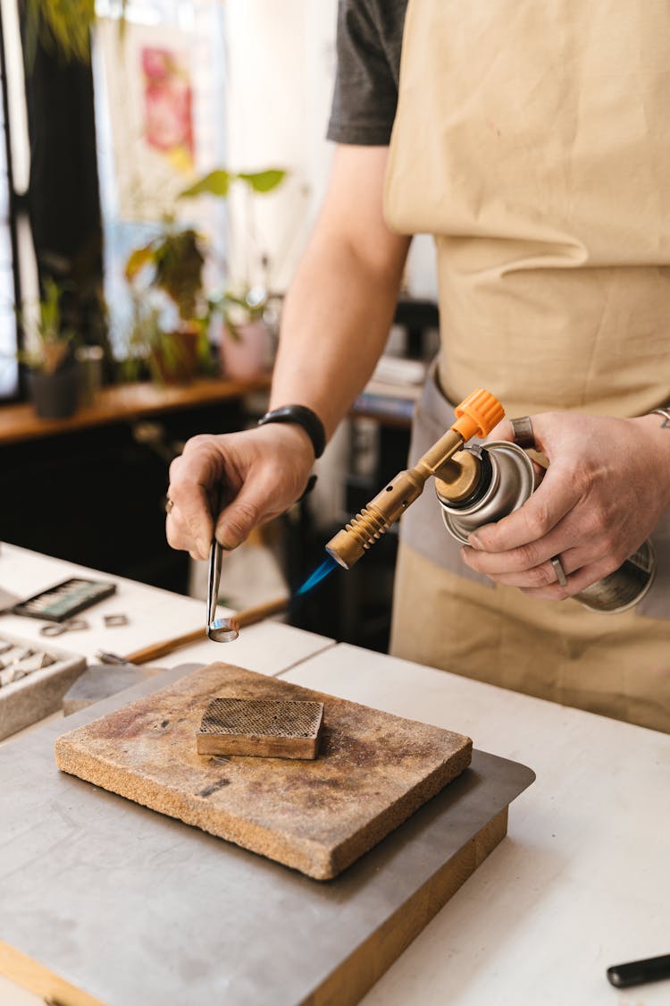 A Person Holding A Piece Of Metal Ring And A Blowtorch