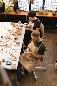 Two artisans crafting jewelry in a workshop setting with tools and materials on the table.