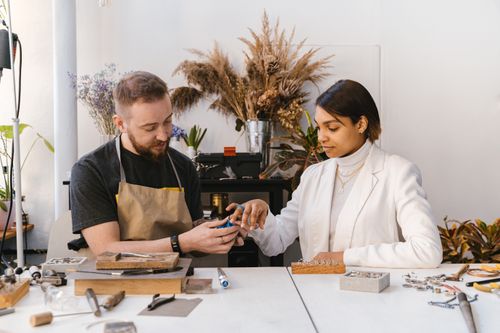 Free Jewelry craftsman showing a piece to a client in an art studio. Collaborative and creative work environment. Stock Photo