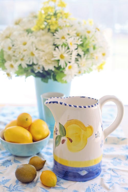 White and Yellow Ceramic Mug Beside Yellow Round Fruits on Blue and White Floral Ceramic Bowl