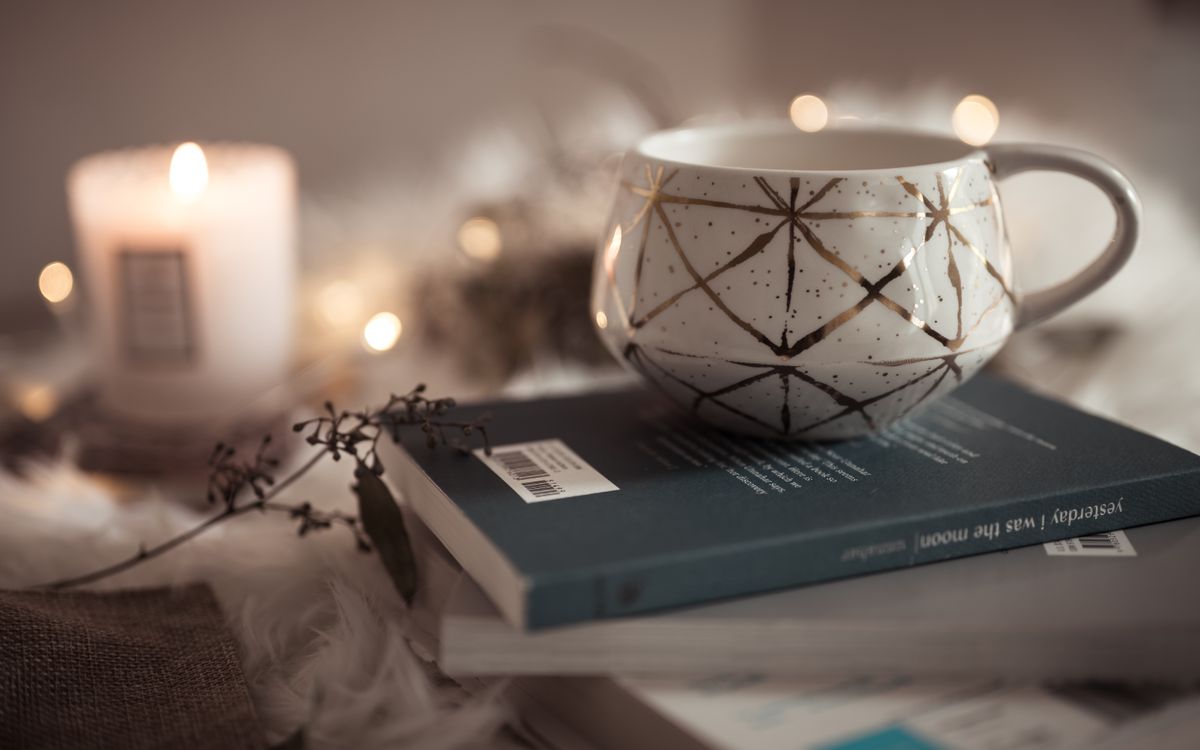 A warm, inviting scene featuring a decorative cup on books, with soft candlelight and a peaceful ambiance.
