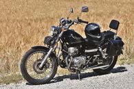 Classic black motorcycle with helmet parked on gravel road against golden field.