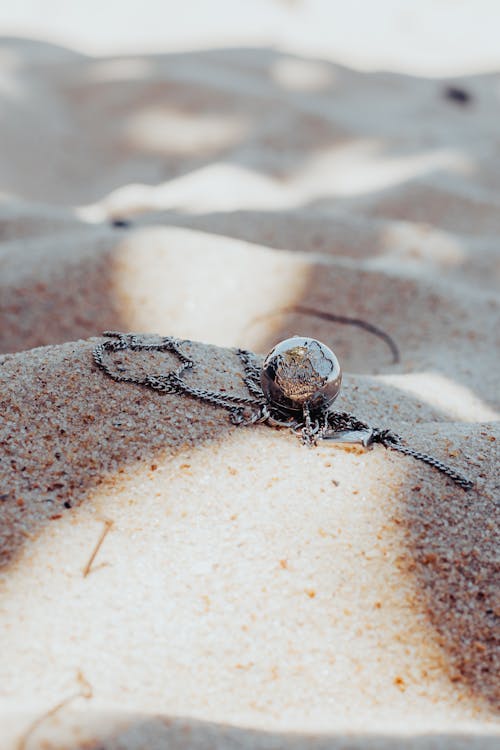 Pendant on Chain Lying on the Sand 