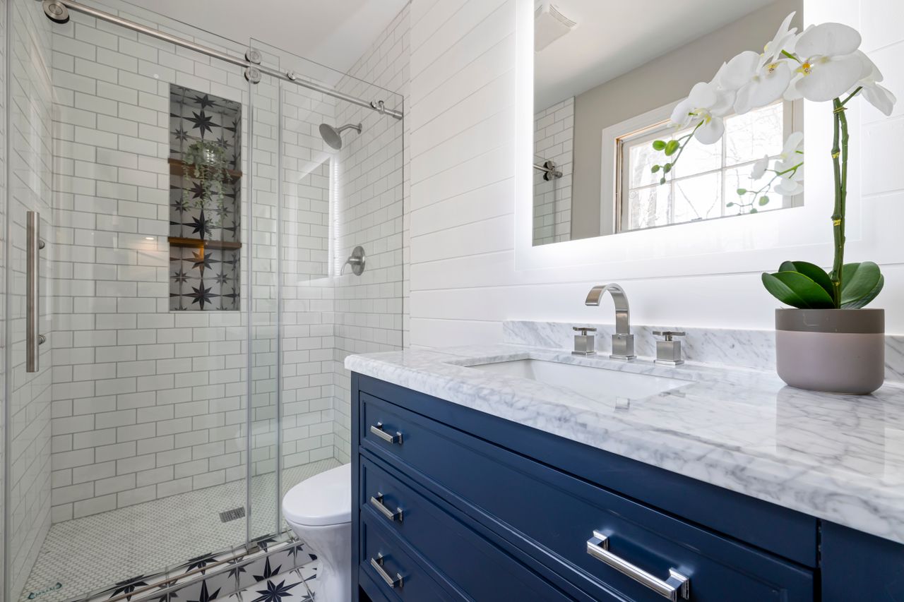 Bathroom with a navy vanity, white subway tile shower, and a patterned tile niche
