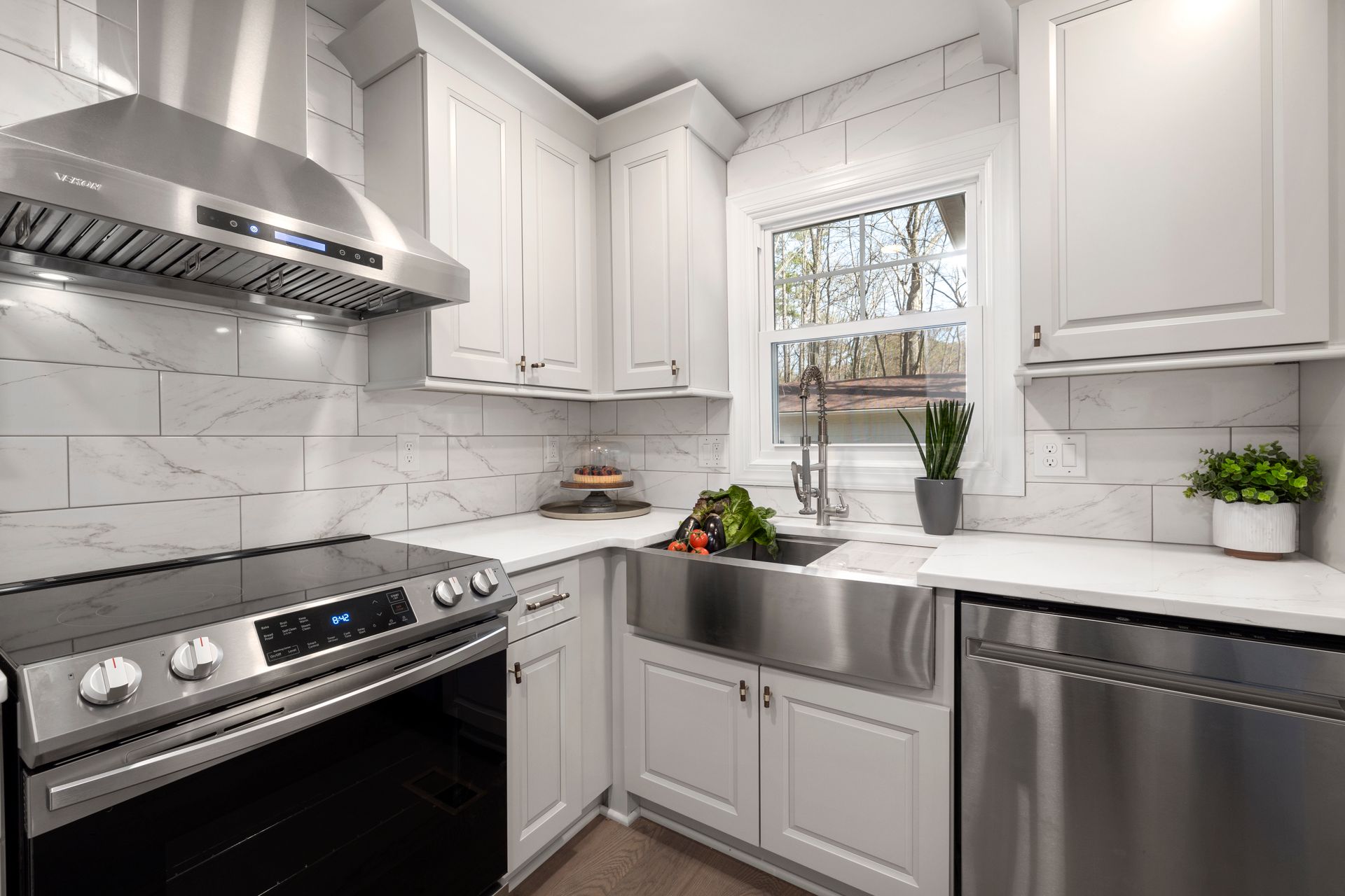 Stylish white kitchen featuring a stainless steel oven, sink, and range hood. Bright and contemporary design.