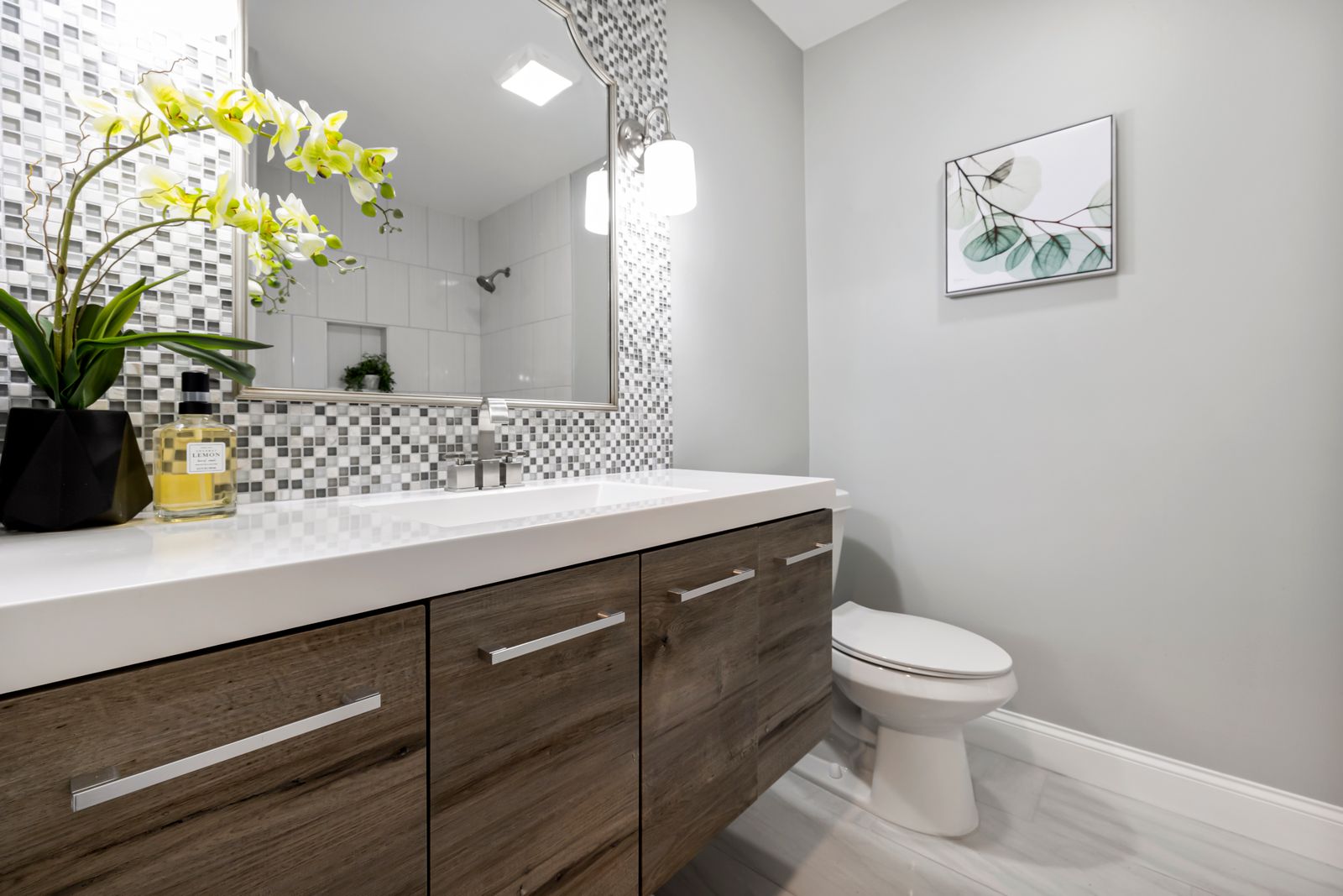 Contemporary bathroom with a timber vanity, white integrated basin, mosaic tile backsplash, large mirror, toilet and orchid plant.