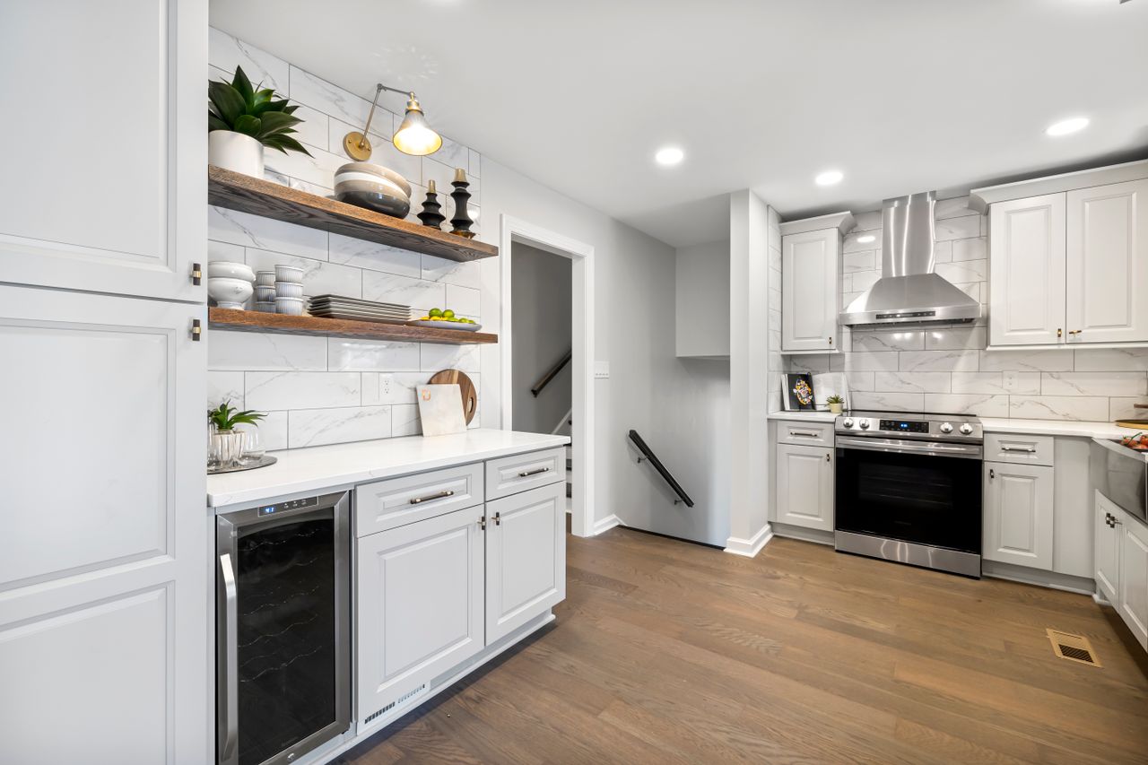 White kitchen with floating wooden shelves, stacked plates and a built-in wine cooler