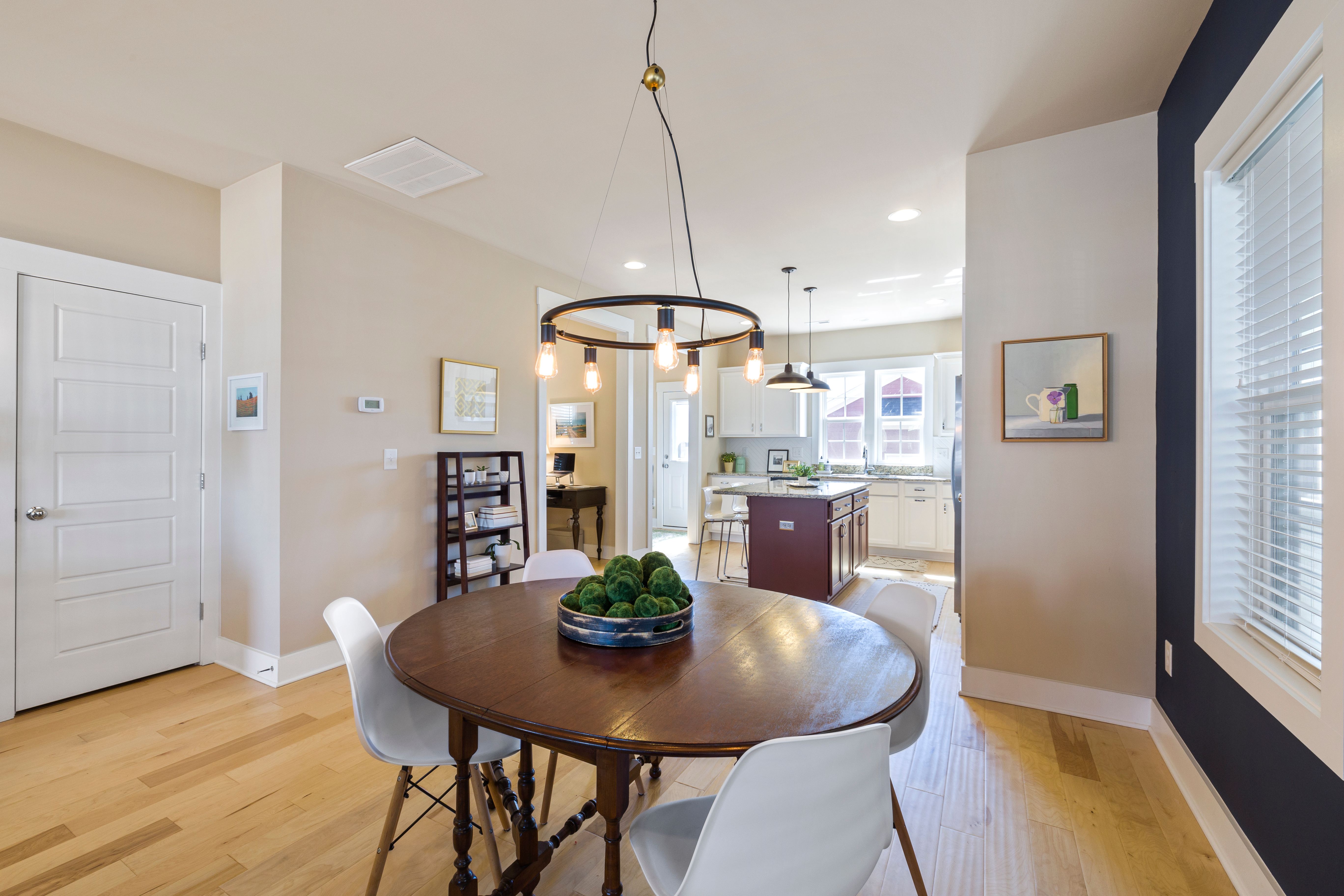 Spacious staged dining area with wooden table, white chairs, and kitchen view