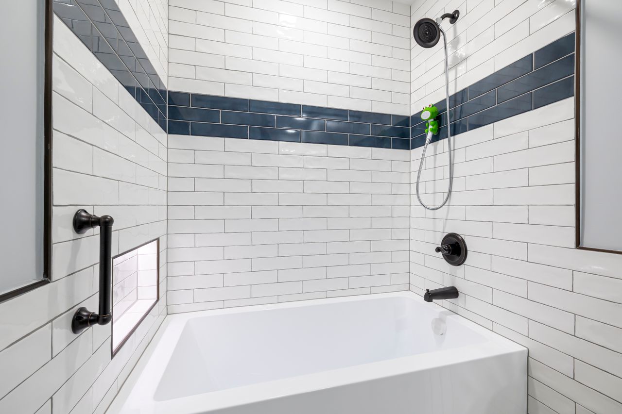 White subway tile tub shower with a horizontal navy tile stripe