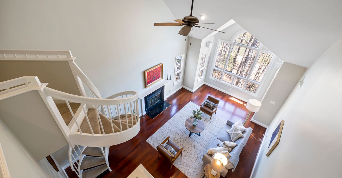 Modern living room with spiral staircase, large windows, and elegant furniture, photographed from above.