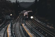 在戏剧性的夜间场景中，一列火车驶近一座被山脉和树木环绕的光线昏暗的车站