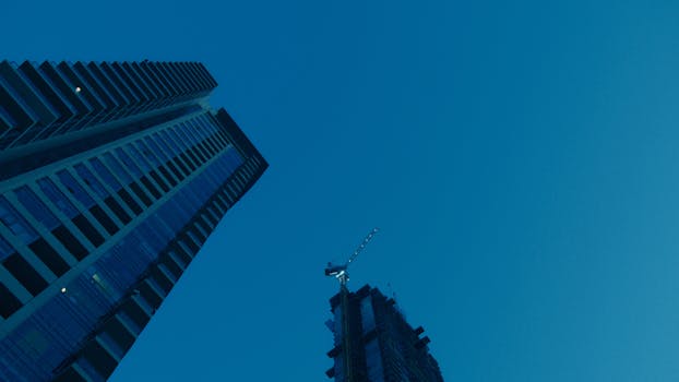 Low angle view of a skyscraper and construction crane against a vibrant blue sky.